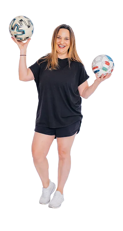 Mag. Birgit Hütter steht lächelnd in Sportoutfit und hält zwei Fußbälle in den H