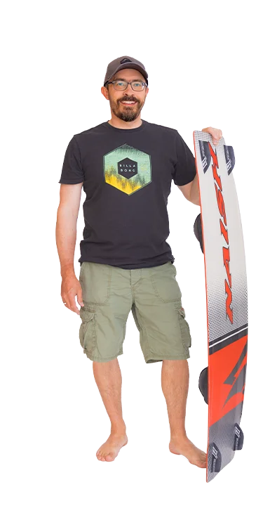 Mag. Gerhard Schüller steht barfuß, trägt ein T-Shirt mit Surfmotiv und hält ein
