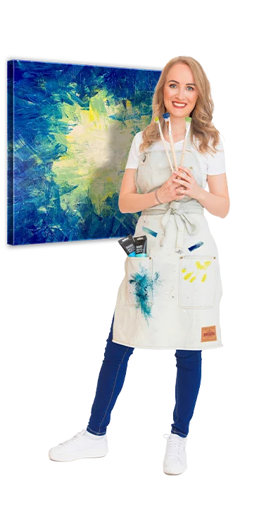 Ricarda Carina Rainer, MSc trägt eine Malerschürze mit Farbflecken, hält Pinsel 