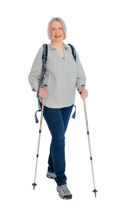 Mag. Sonja Ehrenberger geht mit Wanderstöcken und Rucksack lächelnd auf die Kame